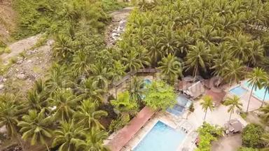热带度假酒店，绿色棕榈树从上面的飞行无人机。 男子游泳在蓝水游泳池度假