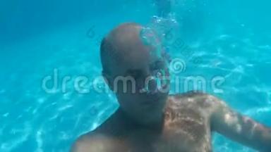 秃头男子潜水水下游泳池和吹气泡。 水下观景人吹着透明的气泡