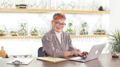 自信的戴眼镜的高级妇女坐在白色办公室的笔记本电脑上