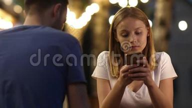 无聊的少女在约会时用电话。 一对夫妇花时间在手机上滚动网页。