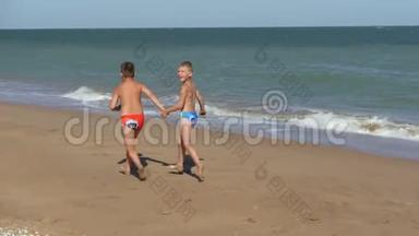 孩子们沿着海岸线奔跑。 海浪在海滩上冲刷。 男孩们牵着手沿着海滩奔跑。 孩子在里面
