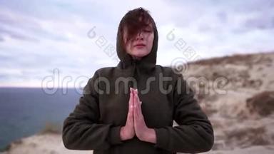 命名或祈祷。 积极的生活方式-一个冷静的女人穿着运动衫，把她的手掌<strong>放在一起</strong>。 在海洋上的悬崖