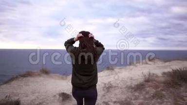 一位年轻漂亮的女运动员在刮风的日子走到悬崖边。 运动运动衫，强风运动衫