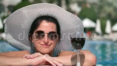 在游泳池享受暑假期间，一位身材矮小的女游客微笑着摆着红酒