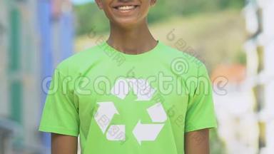 穿着带回收标志的衬衫的男孩微笑着进入相机，推广可重复使用的产品