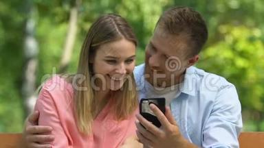 快乐的情侣在智能手机上看有趣的视频，浪漫的公园约会