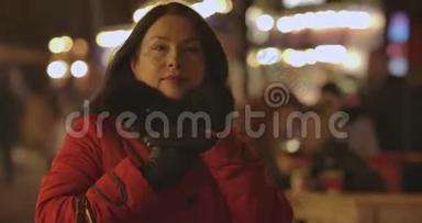 积极的白人妇女穿着红色外套，在晚上沿着城市市场走来走去，环顾四周。 成年女士肖像