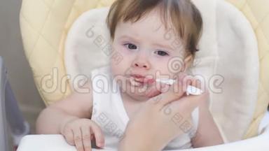 快乐宝宝用勺子吃第一顿饭。 妈妈用小勺子喂宝宝.. 孩子坐在一个现代化的婴儿里