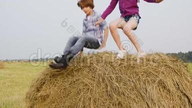 慢动作女孩和男孩在农村的收割场上跳跃干草堆。 快乐的青少年女孩和男孩