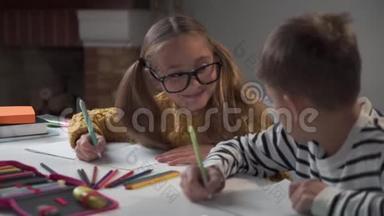 两个高加索同学坐在桌边写练习本。戴眼镜的女孩看着男孩