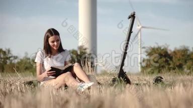 一个迷人的女孩坐在电动滑板车旁边，背景是风力发电站和树叶穿过一个电动滑板车