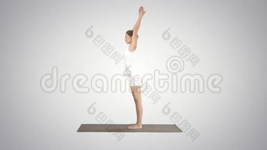 美丽的模特做瑜伽运动，站在Uttanasana，手掌在脚踝后面的梯度背景。