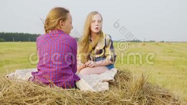 年轻的女朋友坐在村里的农田里的<strong>干草</strong>堆<strong>上</strong>。 无忧无虑的女孩在<strong>干草</strong>堆<strong>上</strong>聊天