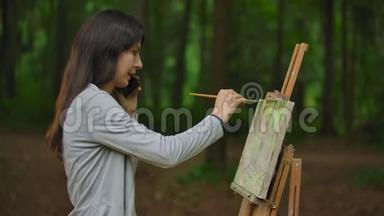 女孩艺术家在公园里画一幅风景画，并通过电话交谈