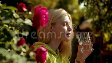 美女从绿色公园的玻璃上喝水。 把金发女孩的画像贴起来。