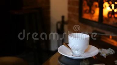 咖啡杯放在有壁炉的咖啡厅或餐厅的桌子上。 桌上闪着火焰. 浪漫的环境