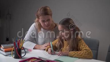 年轻的白种人女导师向可爱的小女孩解释错误。 作业本中的学童书写