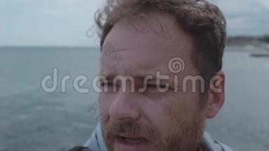 特写一个留胡子的男人的脸，背景是海和云。 风在一个人4K中长出头发。 4k视频