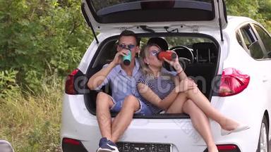 可爱的夫妇喝热茶从热水瓶坐在汽车后备箱。