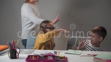 戴眼镜的白人女孩和她的男同学用五颜六色的钢笔打架。 成年女人过来安抚他们