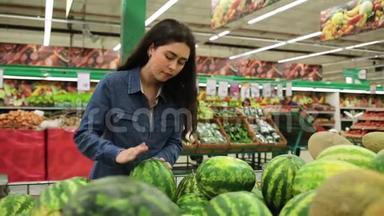 在超市购物。 年轻的美女在水果店的货架上摘西瓜