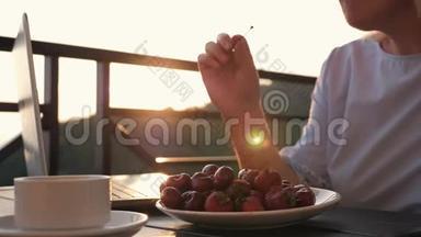 一个女人在日落时吃成熟的Krasnfe浆果。 草莓和樱桃<strong>放</strong>在火炬里，<strong>放</strong>在<strong>桌子上</strong>，<strong>放</strong>在阳光下