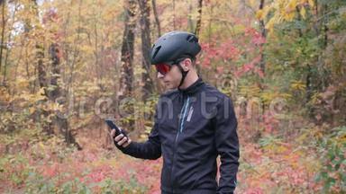 在秋季城市公园的智能手机上自拍的骑自行车服装的年轻迷人的Sports家伙。 拍摄照片的专业自行车手
