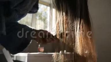 布鲁内特女孩吹<strong>干湿</strong>发背景下的太阳`光线靠近窗户。 女人正在给头发做造型