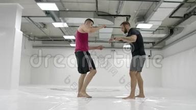 MMA战斗机练习摔跤技术。 白色大厅和榻榻米上的摔跤手。 一个穿红色T恤的男人和一个穿