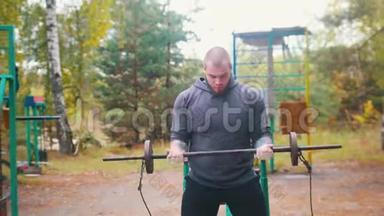 一位纹身男健美运动员用<strong>小哑铃</strong>抽手在户外运动场上训练-秋天