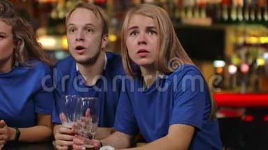 一群球迷情绪激动地在电视上的一家酒吧里观看体育节目，他们穿着啤酒，男女穿着蓝色T恤