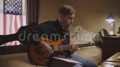 <strong>专心</strong>致志的年轻人坐在床上弹吉他，在家写音乐