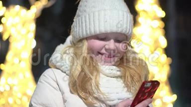 一个美丽的金发女人在冬天装饰着圣诞<strong>节</strong>的街道上的智能<strong>手机</strong>里聊天