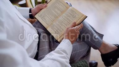 一个穿着白色衬衫坐在扶手椅上的无名男子<strong>正在看书</strong>。