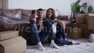兴奋的白种人夫妇坐在他们的新房子的地板上，自拍或给他们的朋友打视频电话
