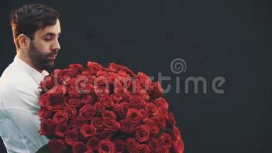 年轻男子出现在黑色背景与大束红色玫瑰。 他沉重地叹了口气，看着