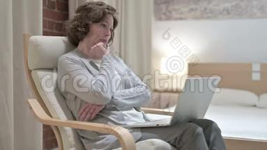 老妇人在沙发上思考和工作笔记本电脑