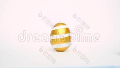 复活节彩蛋在滚动，在白色的桌子上互相碰撞。鸡蛋时髦的颜色经典的蓝色，白色和金色。快乐