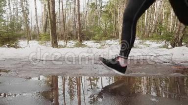 冬季公园慢跑时腿踩水坑的慢动作视图。