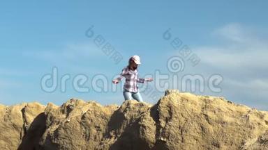 一个年轻的女人走在远处的岩石上。 戴帽子的女孩小心翼翼地沿着岩石走。 天气晴朗