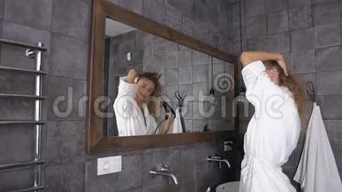漂亮的金发女人，穿着白色浴袍，在家里的浴室里，长发在镜子前晾晒头发