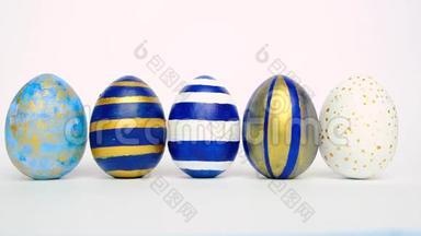 复活节彩蛋在<strong>滚动</strong>，在白色的桌子上互相碰撞。鸡蛋时髦的颜色经典的<strong>蓝色</strong>，白色和金色。快乐