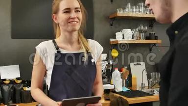 一位漂亮的女咖啡师拿着平板电脑和微笑的顾客点餐的画像