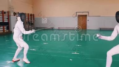 两名身穿白色防护服的年轻女子在学校体育馆接受击剑训练