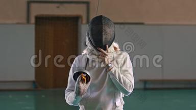 一个金发的年轻女击剑运动员摘下了一顶戴着剑的头盔