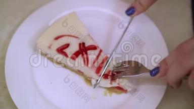 白色盘子上的奶酪蛋糕。 女人用刀切进去，用叉子取一块。 美味的最爱糕点。