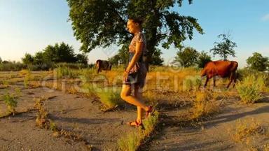 穿着短裙的牛仔女郎在夕阳下的牧场上<strong>远离</strong>镜头，靠近长满沥青的炎热的乡村