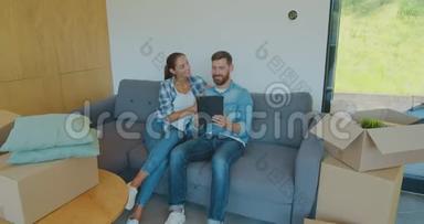 幸福的一对房客坐在沙发上，在新房子<strong>搬</strong>家的日子里使用数字平板电脑，男<strong>人</strong>和女<strong>人</strong>都放松了