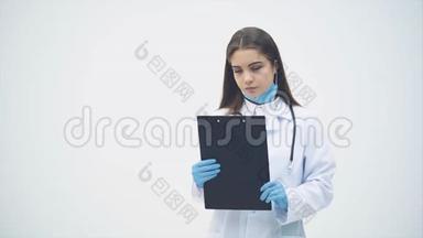 年轻的女<strong>实习生</strong>站在医用制服上，拿着剪贴板，看着镜头，表情严肃。