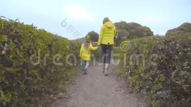 回到快乐的白人女儿和她快乐的母亲在绿色的灌木丛中跳跃。 一个大黑人